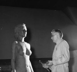 Dr. Harry Wann stands in a studio facing the nude figure of a woman he is sculpting