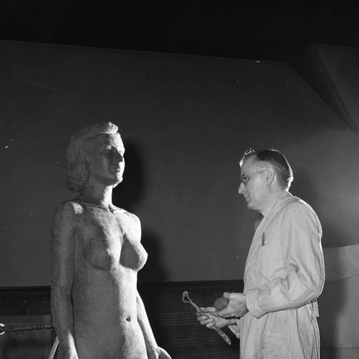 Dr. Harry Wann stands in a studio facing the nude figure of a woman he is sculpting