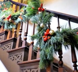 A stairway banister made of wood. It is looped with evergreen swag for the Holiday Tea.