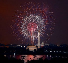 Red, white, and blue fireworks explode over a body of water