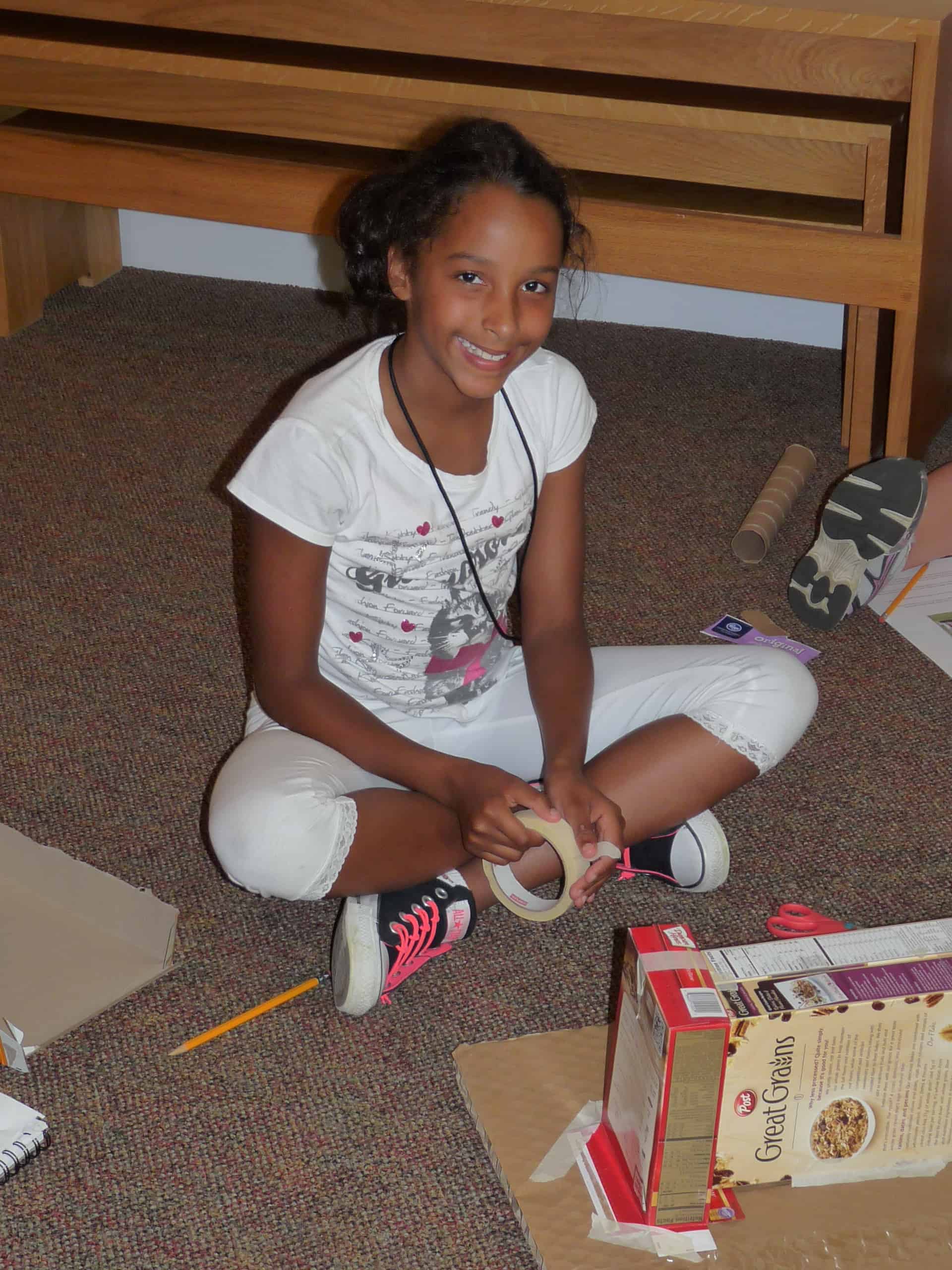 A young Black girl sits cross-legged on the floor working on an ArchiCamp project