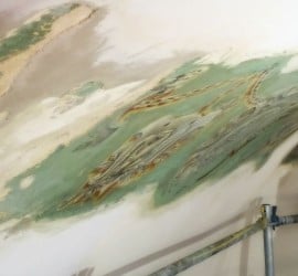 Associate Director Amanda McGuire stands on scaffolding, inspecting the frieze that is being uncovered.