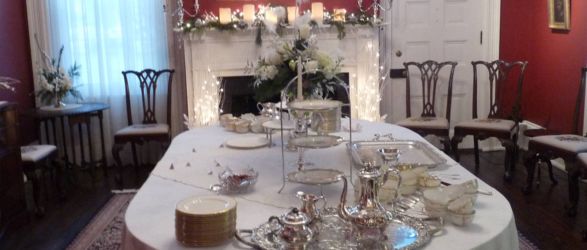 A dining room table set with fancy tea settings. A fireplace is in the background.