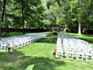 A wide expanse of grass and trees with white chairs in rows for weddings.