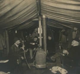 The inside of a houseboat. Lew Wallace sits in conversation with several other men.