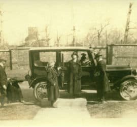 A man stands in front of an antique car with General Lew Wallace's Study building and wall in the background.